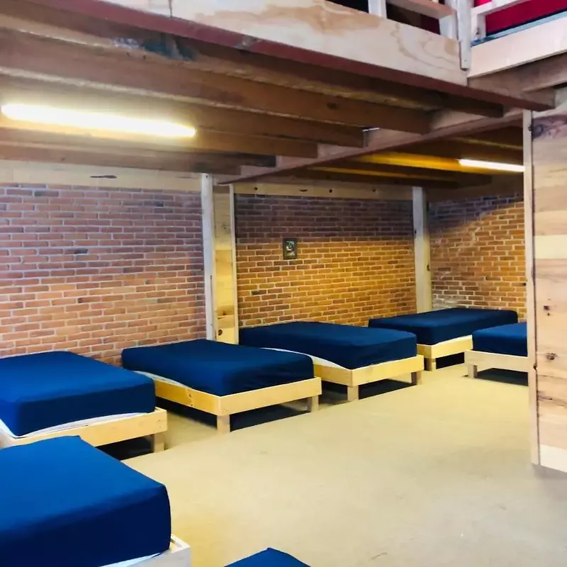 Cabaña tipo albergue con camas individuales divididas en dos estancias amplias.